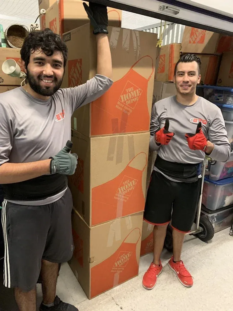 Two smiling ETG movers giving a thumbs up next to stacked moving boxes