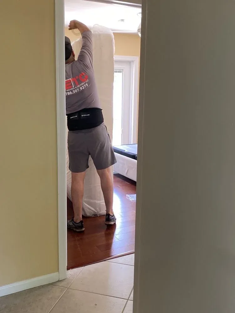 ETG mover in company shirt carrying a mattress through a doorway